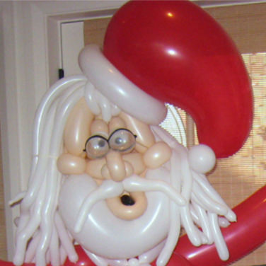 Santa face close-up. He has long white hair with a santa hat that sits comically off center, with funky eyeglasses.